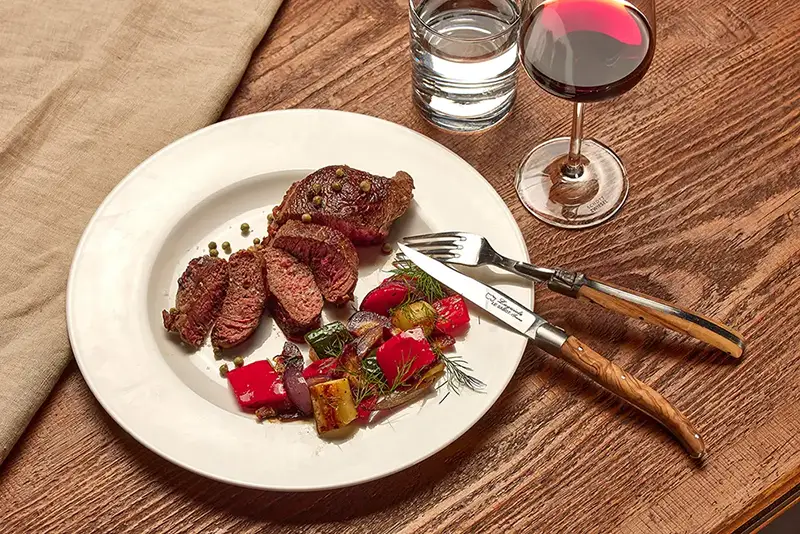 Bisonsteak angerichtet mit gegrilltem Gemüse auf einem Teller mit einem Glas Rotwein